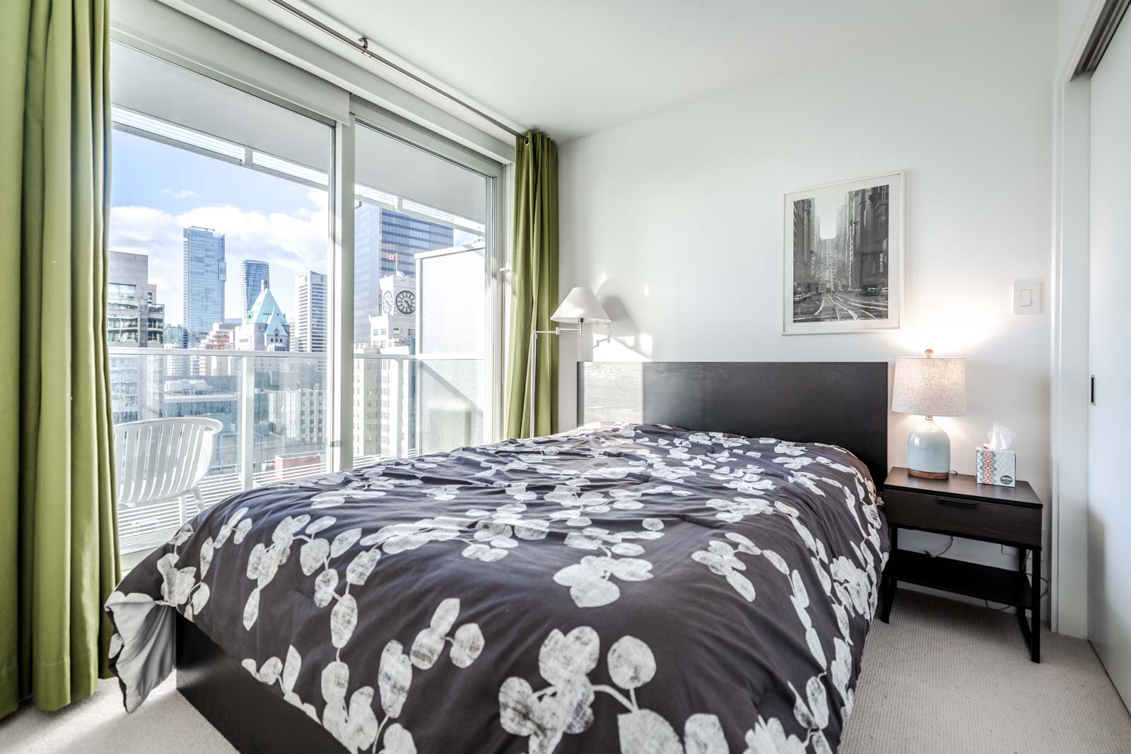 Bedroom with green curtains and black-and-white floral bedspread and view of Downtown Vancouver.