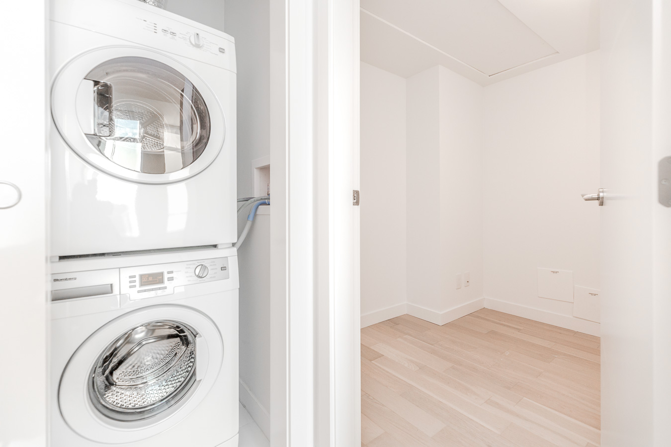 washer and dryer stacked and partial view into adjacent empty room