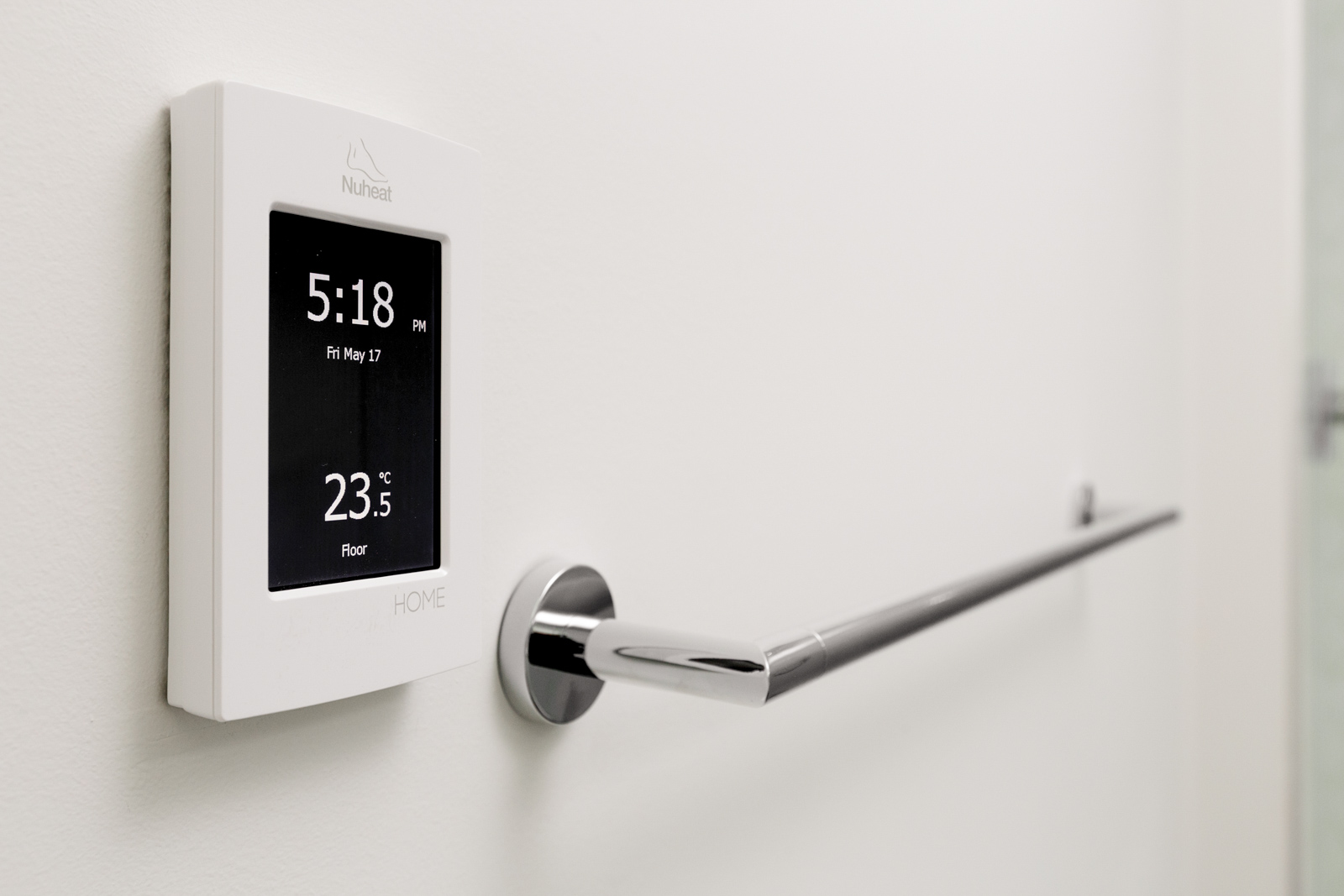 A digital thermostat displaying 5:18 PM and 23.5°C is mounted on a white wall beside a chrome towel bar.