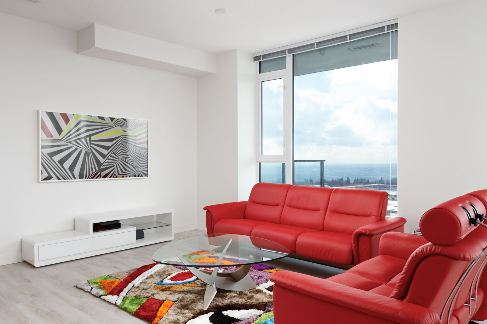 Living area with vibrant red couches and a bay window offering waterfront views from Burnaby rental penthouse.