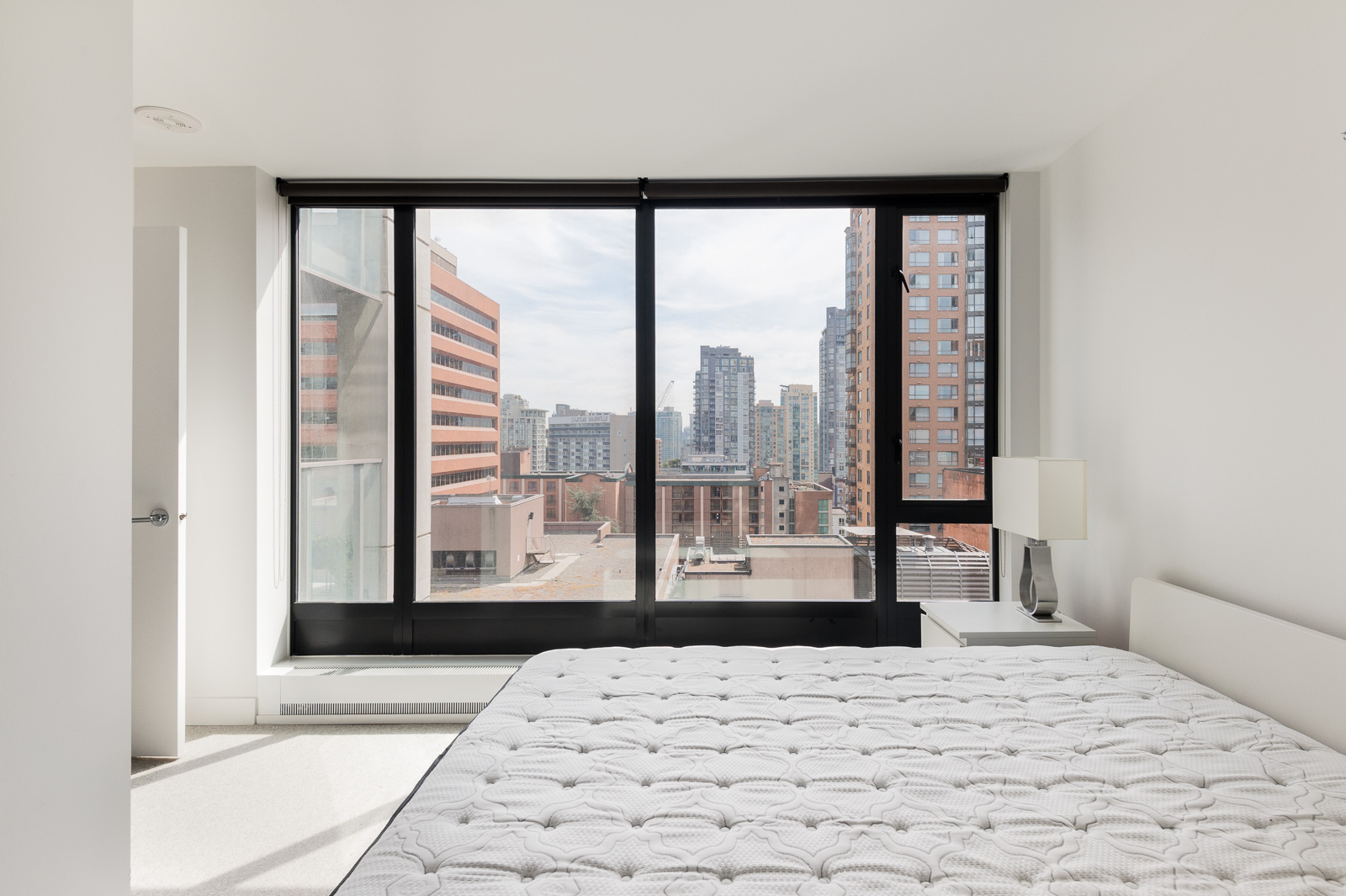 Bedroom in luxury rental with floor-to-ceiling windows offering view of Vancouver.