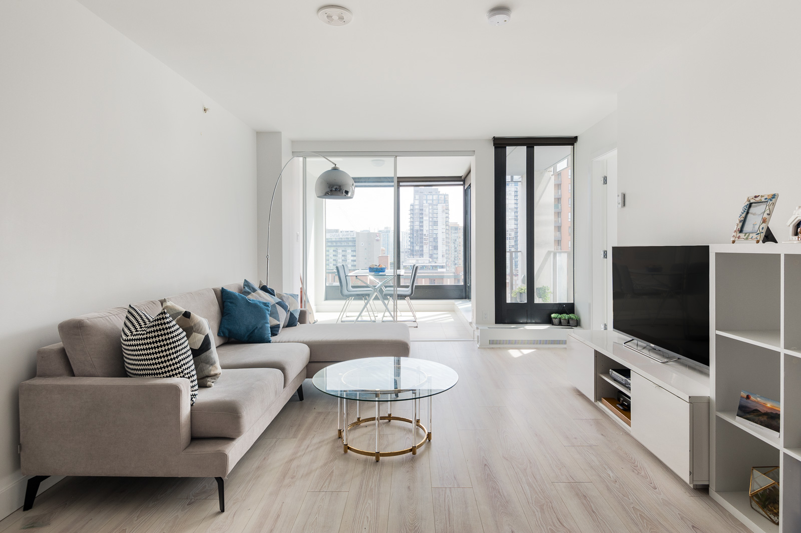 Living room with ash hardwood and grey couch facing television inside Vancouver luxury condo rental.