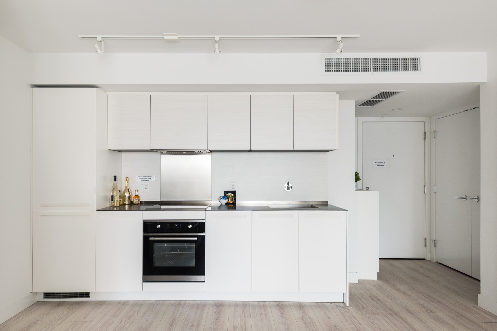 Kitchen decorated in ash hardwood and white cabinetry with built-in stove top oven in Vancouver luxury condo.