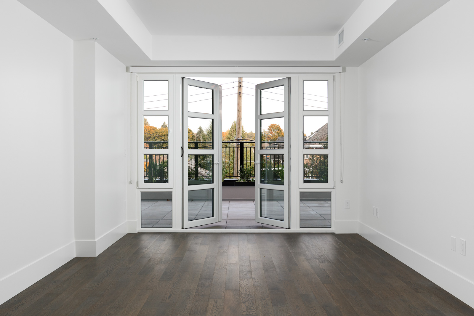 Living room of condo with dark brown hardwood floors with open window doors onto patio