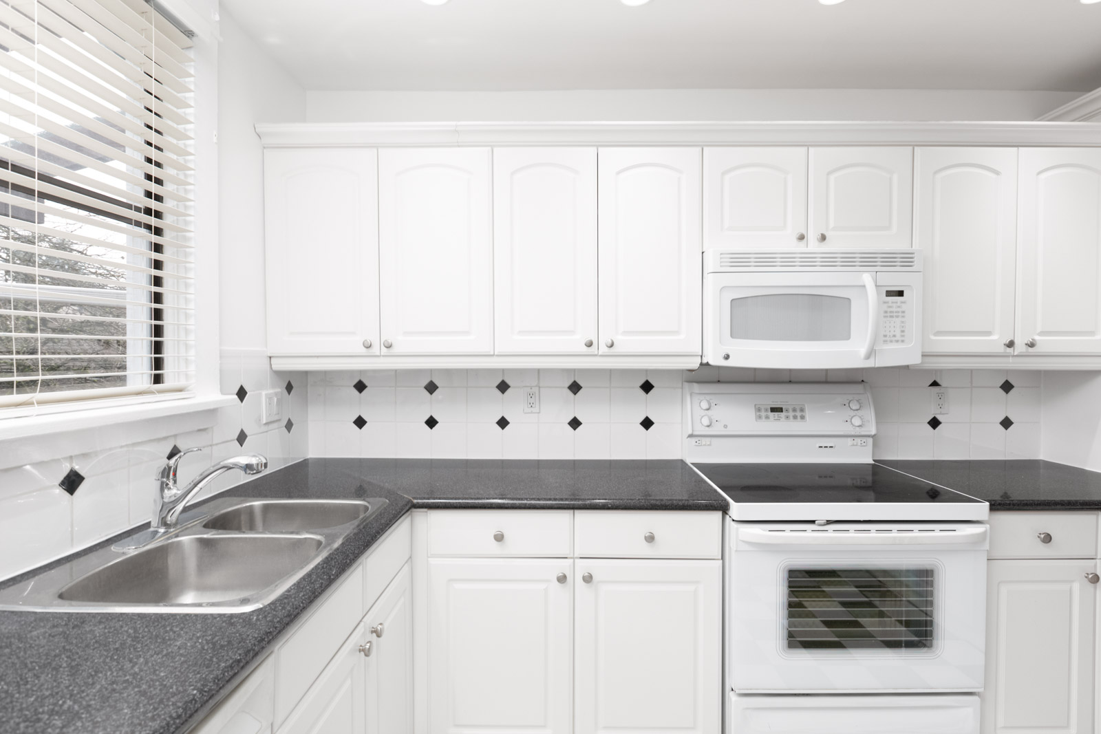 Kitchen with white cabinets with white oven and dark stovetop on left along with over the top white microwave