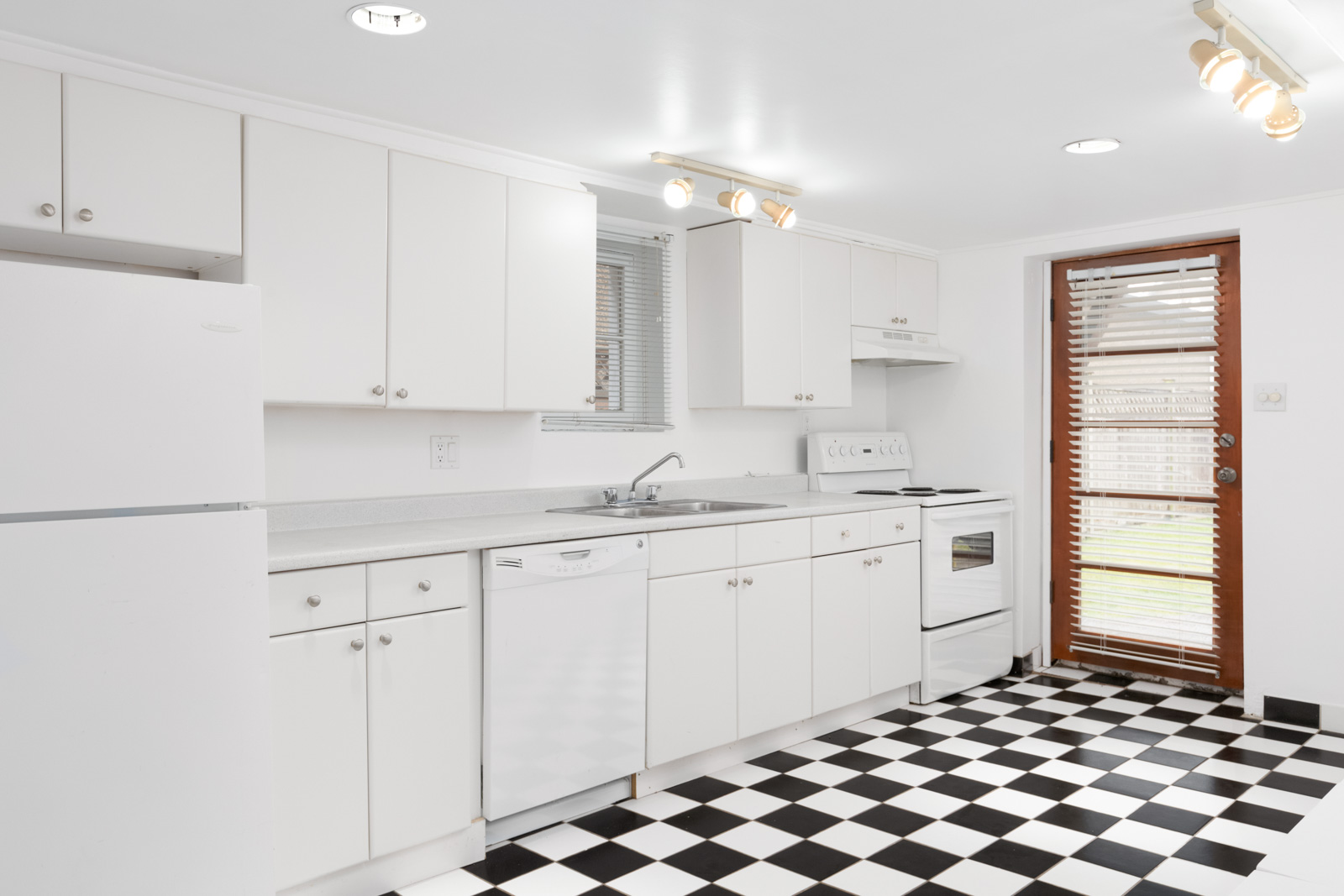 kitchen with checkered black and white floor tiles and white cabinets with door to outside on right