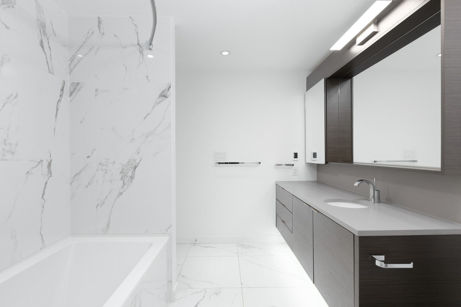 bathroom with bathtub on left and counter and mirror on right and white tiling and floors