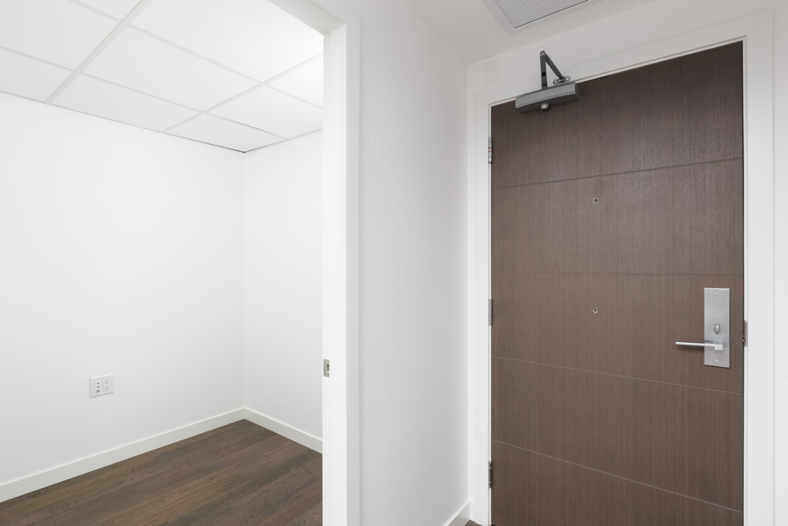 storage room on left and dark wood entrance door on right from inside a modern condo with white walls