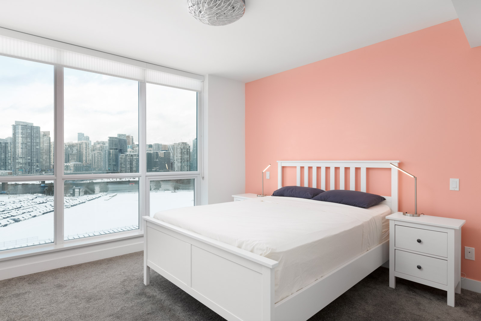 white bed with white bedding and beige wall on the right and floor to ceiling windows on the left