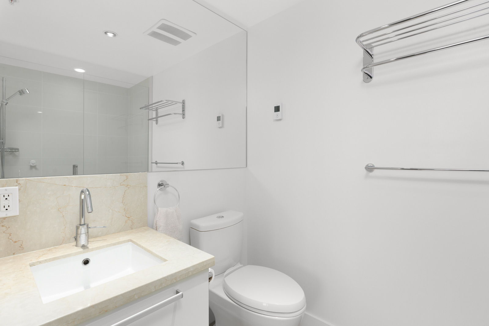 white bathroom with vanity sink and mirror on left toilet in the middle and white wall on right with high towel rack