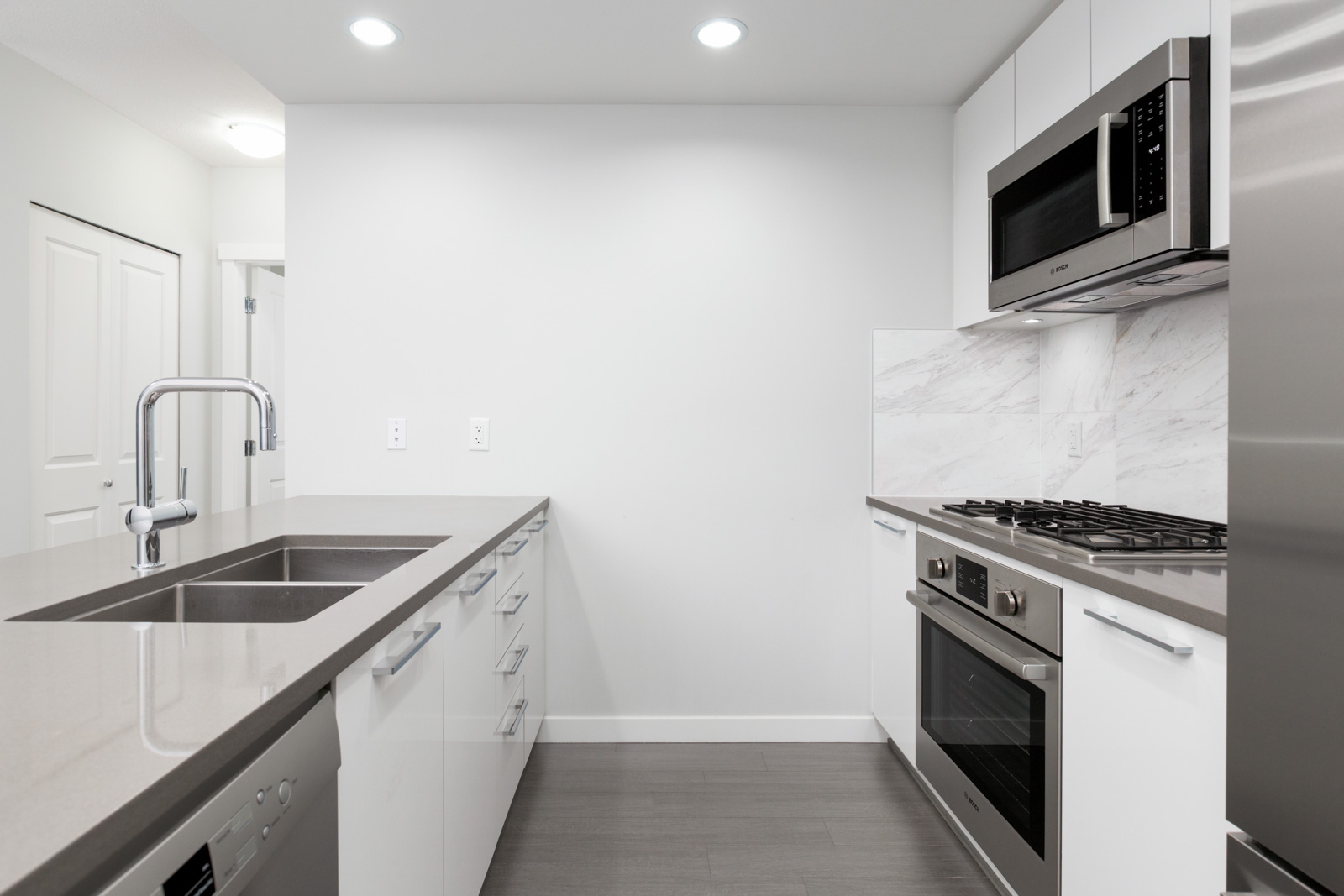 side view of condo kitchen with island counter on left with faucet and sink and dishwasher and kitchen wall on right with stainless steel stove and oven and stainless steel over the top microwave