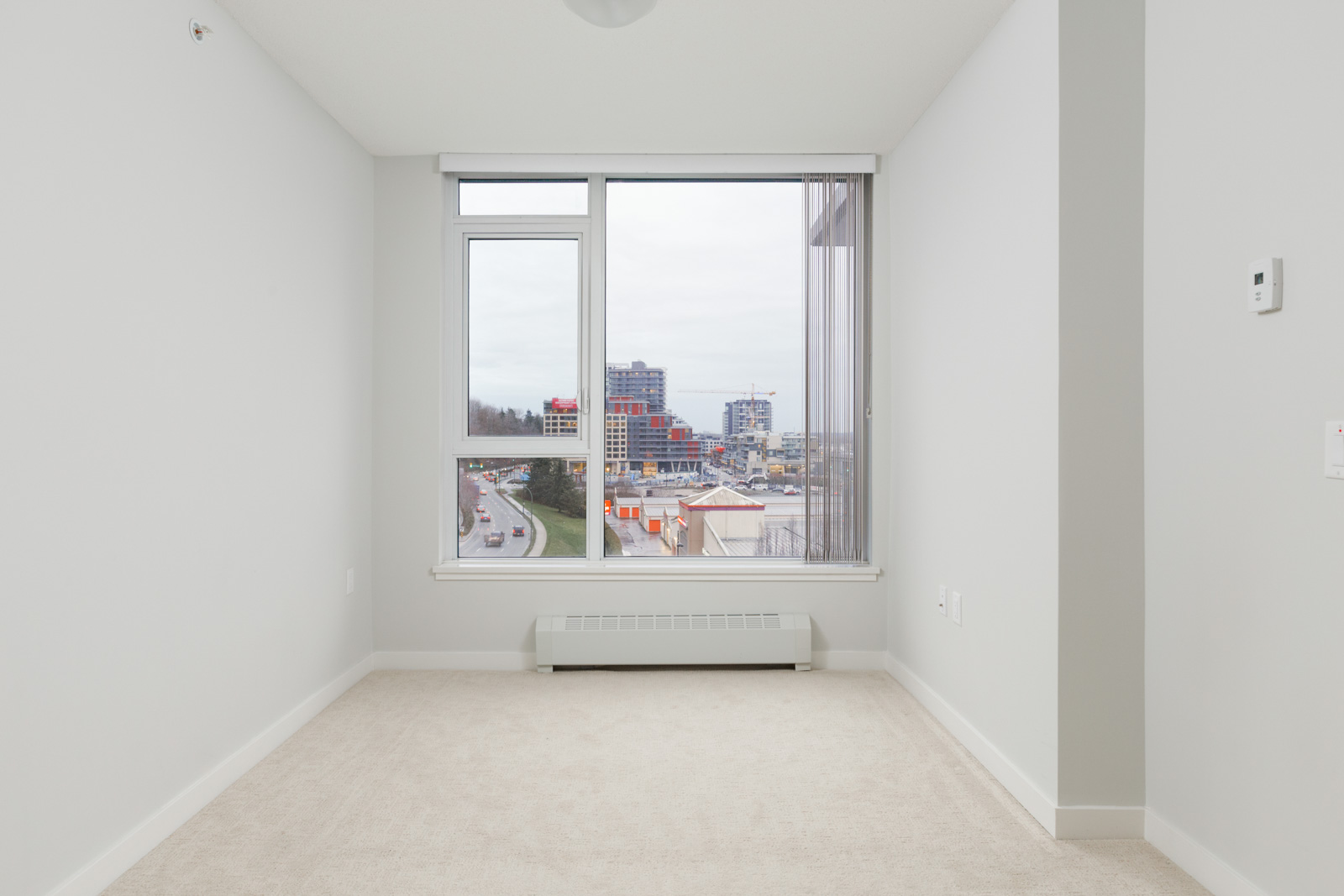 empty room in condo with white walls and carpeted floors and straight view of outside through large windows