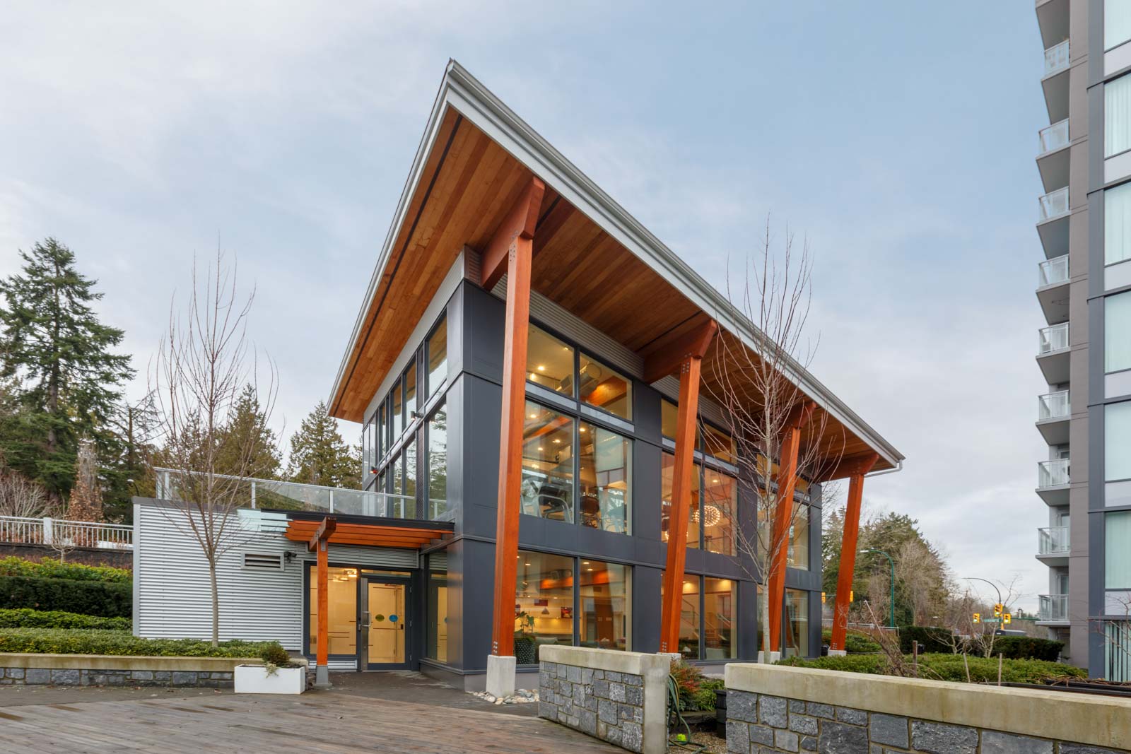 view of common area building exterior structure with large windows and modern wooden roof and high rise portion on the right as part of the rhythm condo building in river district fraserview of vancouver