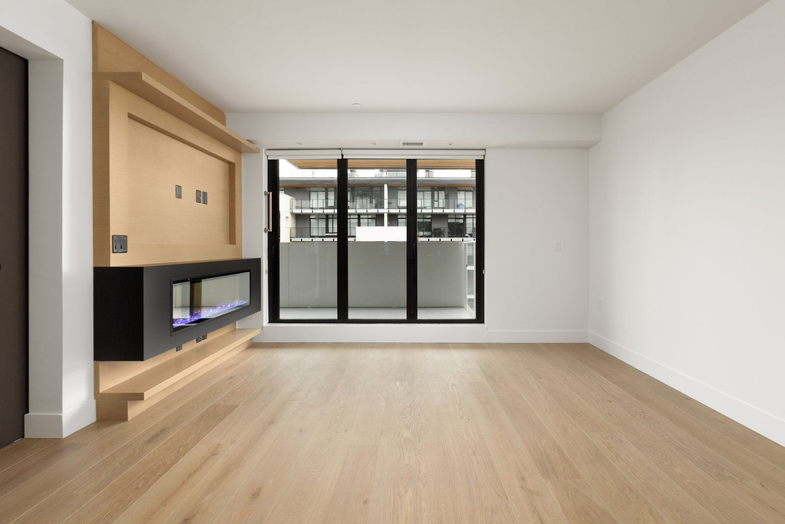 rental condo living room in mount pleasant vancouver with fireplace on left and hardwood floors and three floor to ceiling windows opening to balcony in background