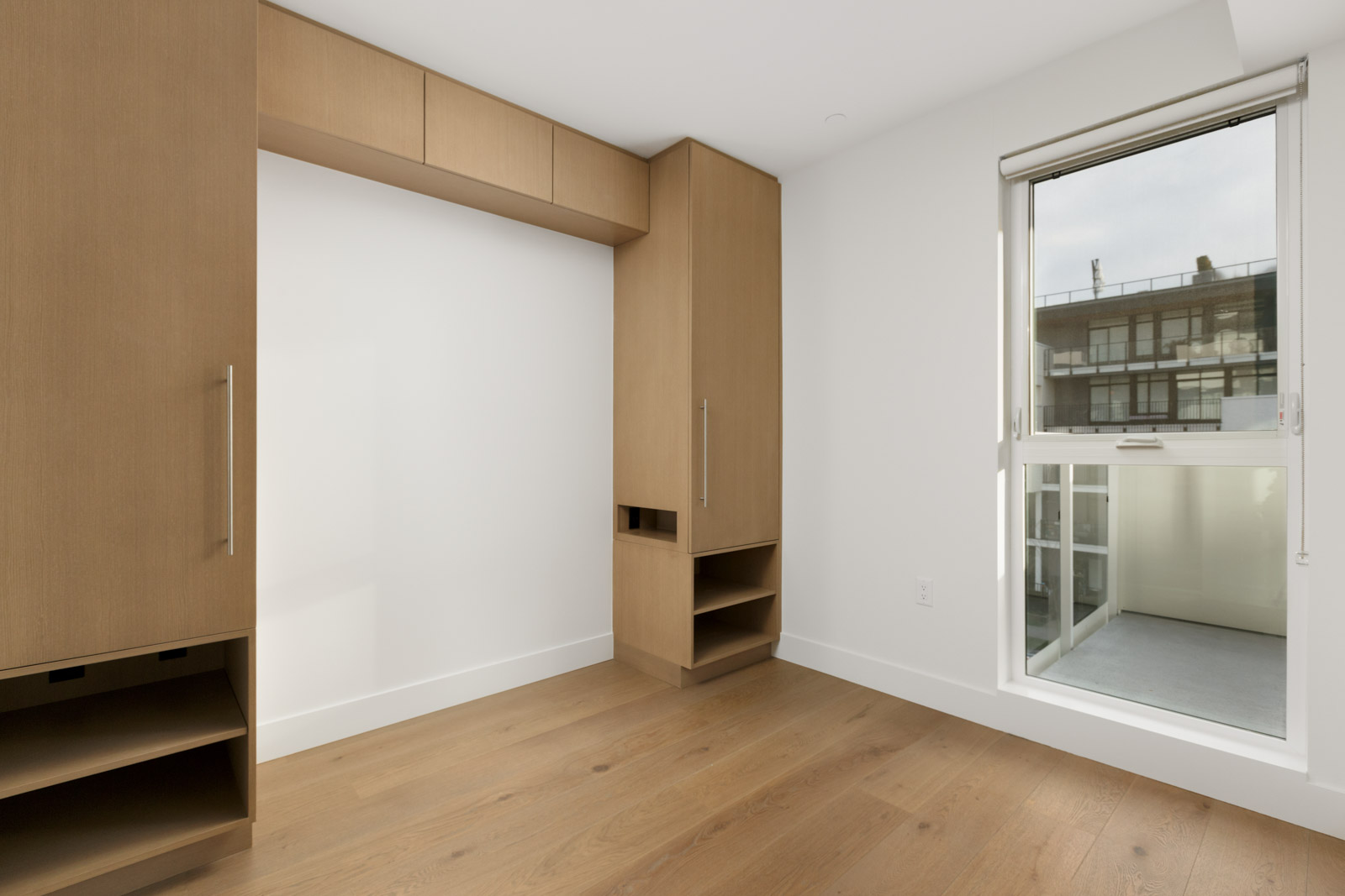 diagonal view of livig room space with partial window on right and white wall on left framed with wooden shelving in vancouver rental condo in mount pleasant