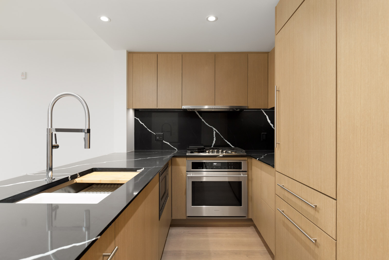 side view of vancouver condo kitchen at shift by aragon with kitchen island with faucet on left and stove top and oven in centre and kitchen cabinets above and on the right