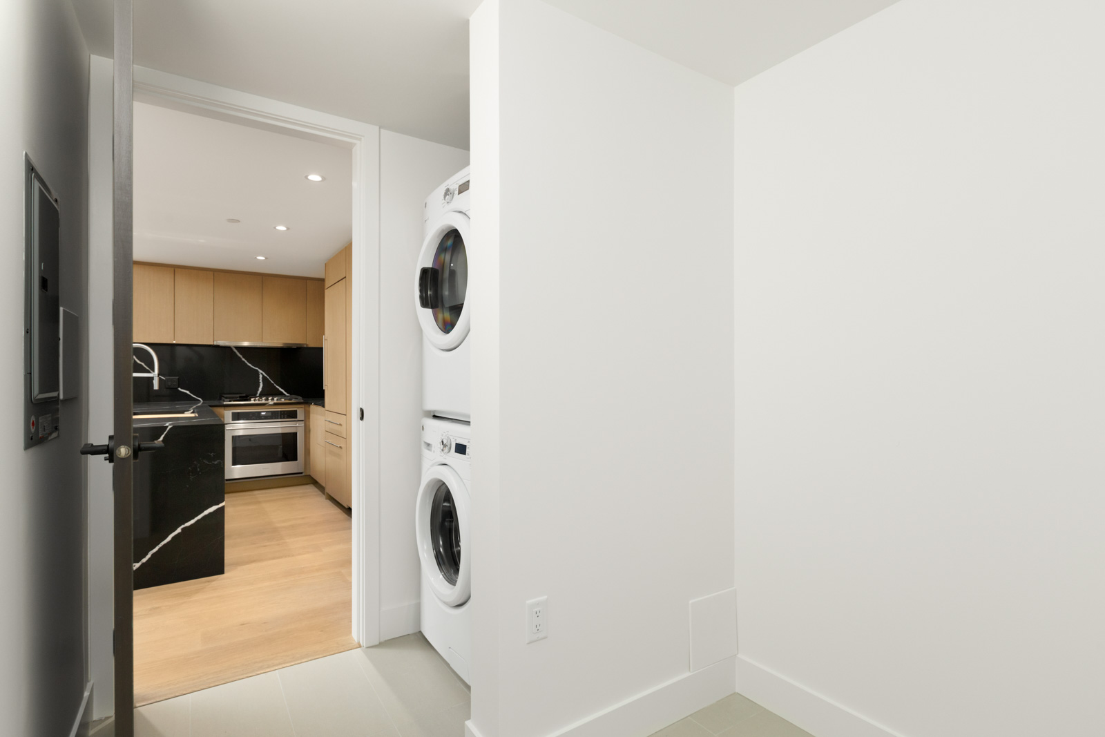 partial view of stacked white washer and dryer in vancouver rental condo in mount pleasant managed by birds nest properties at shift in mount pleasant vancouver with kitchen on left and white wall on right