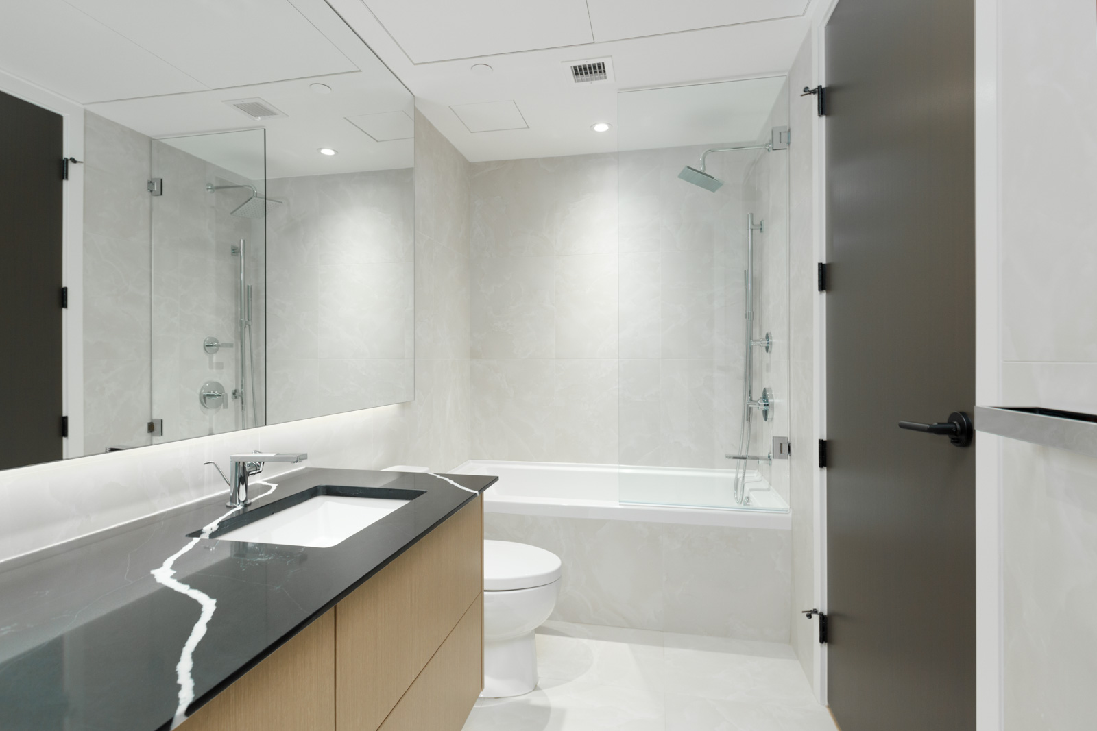 bathroom of vancouver condo managed by birds nest properties with sink and counter on left and toilet in middle and tub and shower in background with white tiling