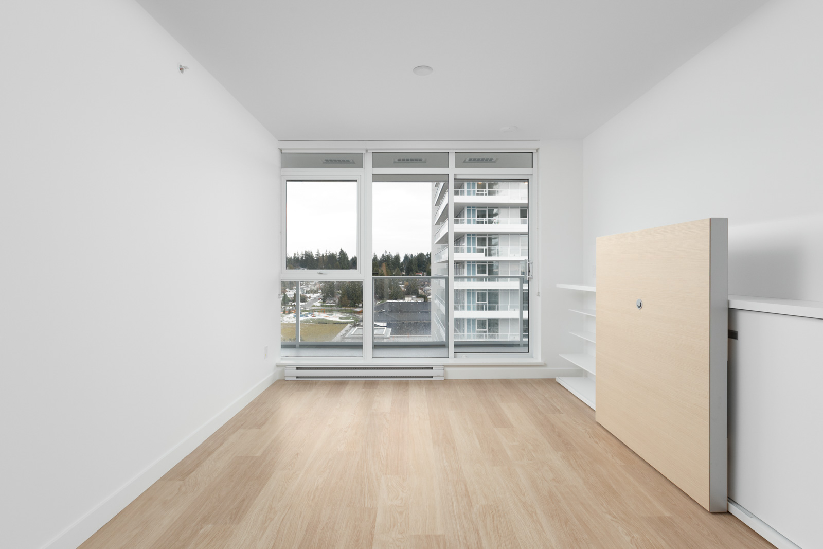 view of empty condo unit with hardwood floors and white walls looking straight out floor to ceiling window with building across the street on right side