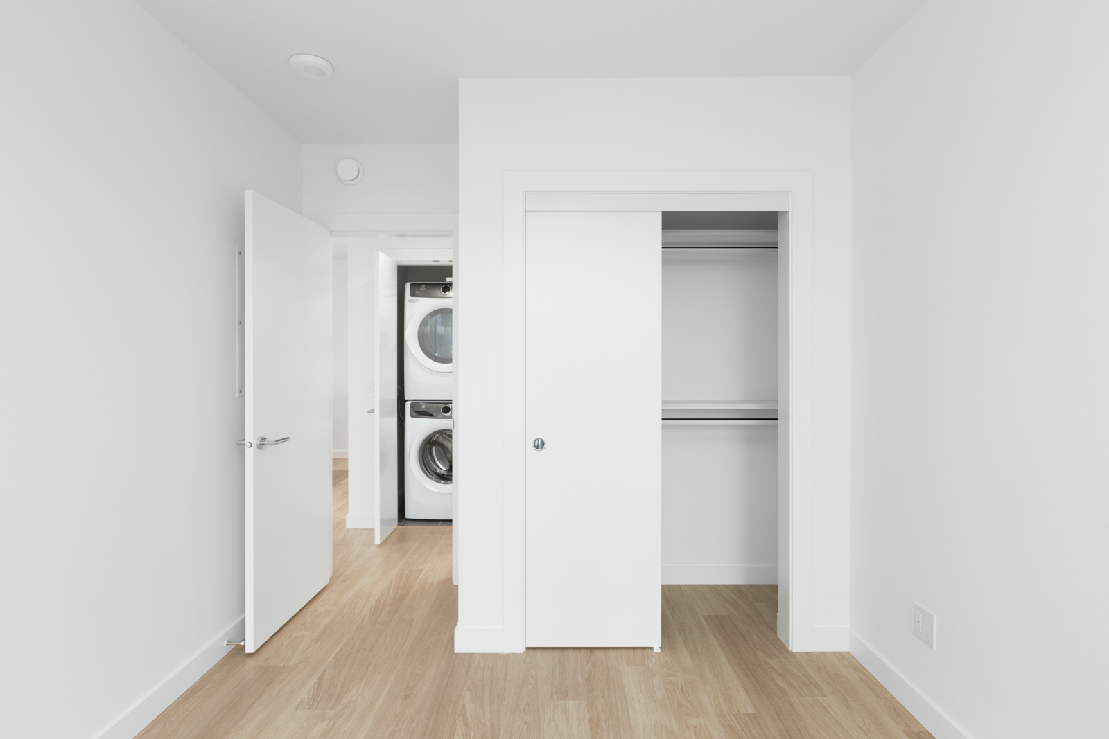 view in bedroom of opened closet space on right and opened laundry closet in background on left with stacked white washer and dryer