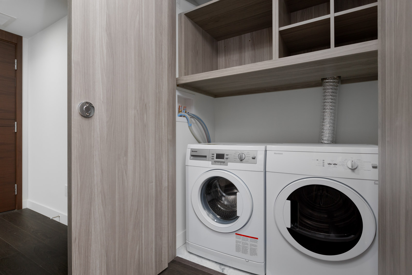 white side by side washer and dryer with door on left and shelving above at concord gardens south estate in richmond