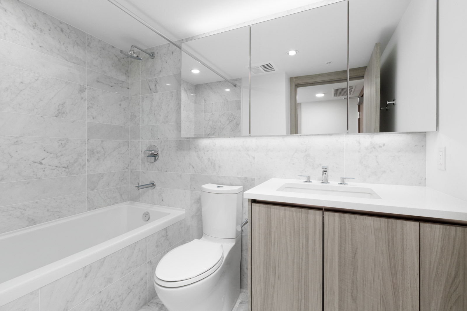 bathroom with tub and shower on left toilet in and vanity on right with mirrors above in bathroom of empty condo at concord gardens on hazelbridge in richmond