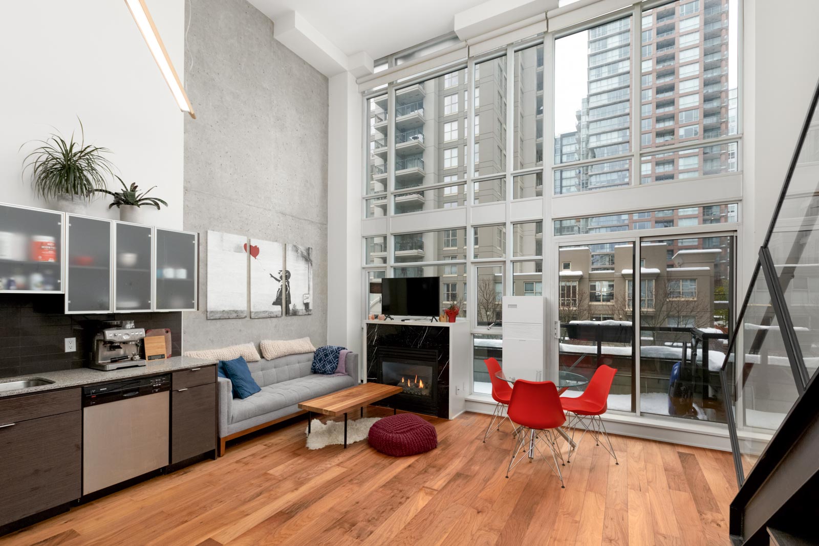 living room of condo with hardwood floors kitchen on left and floor to ceiling windows on right with view to buildings across the street
