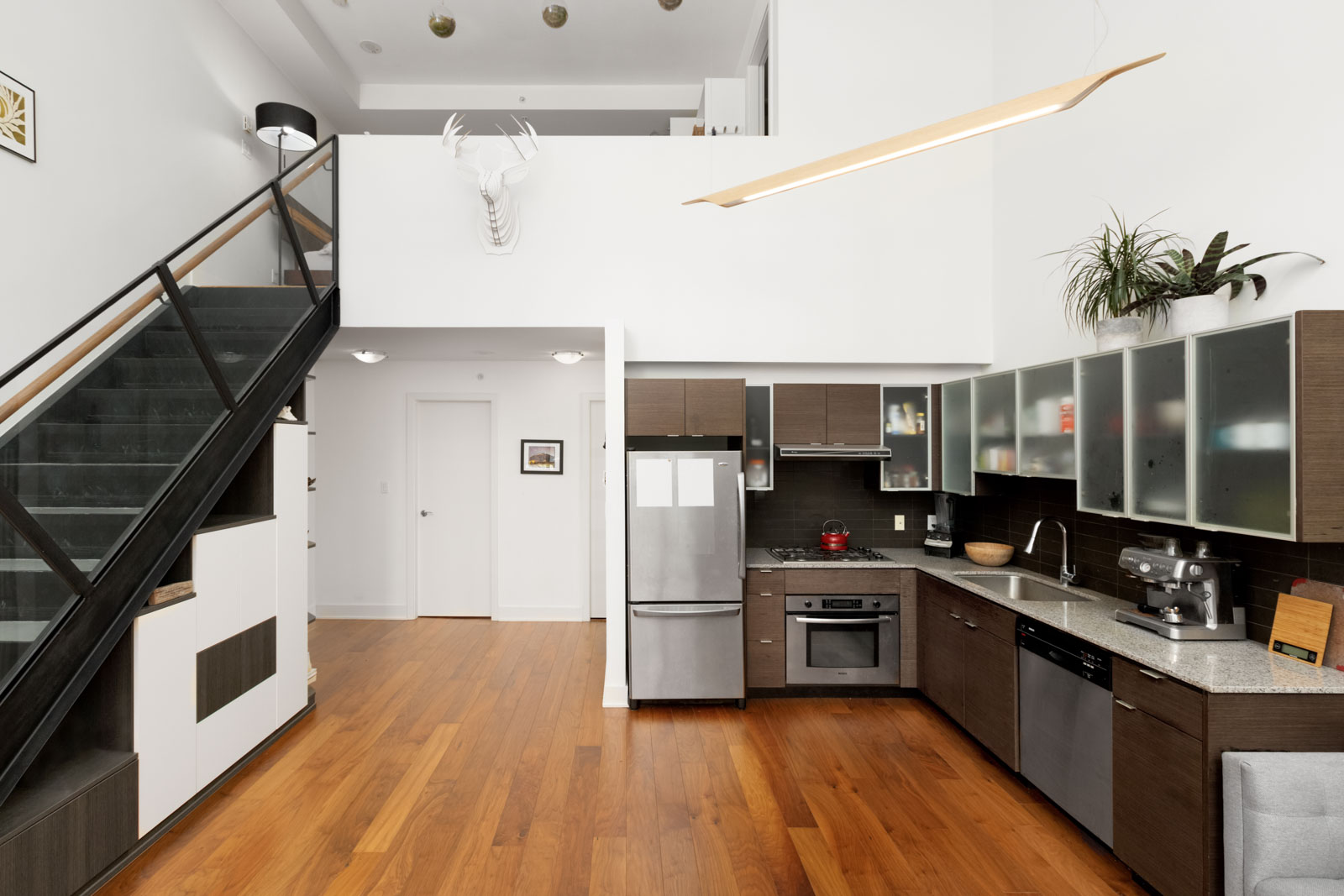 view of two levels in loft apartment with hardwood floors ktichen on right and partial view of stairs on left and white walls above