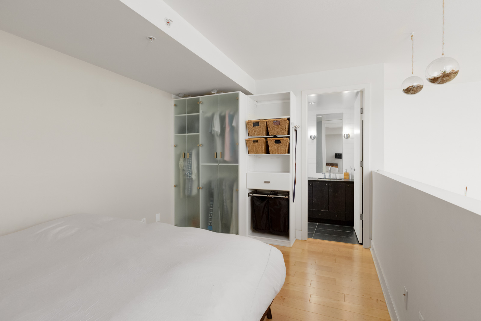 partial view of bed on left in bedroom with hardwood floors looking at closet and doorway looking out to rest of condo