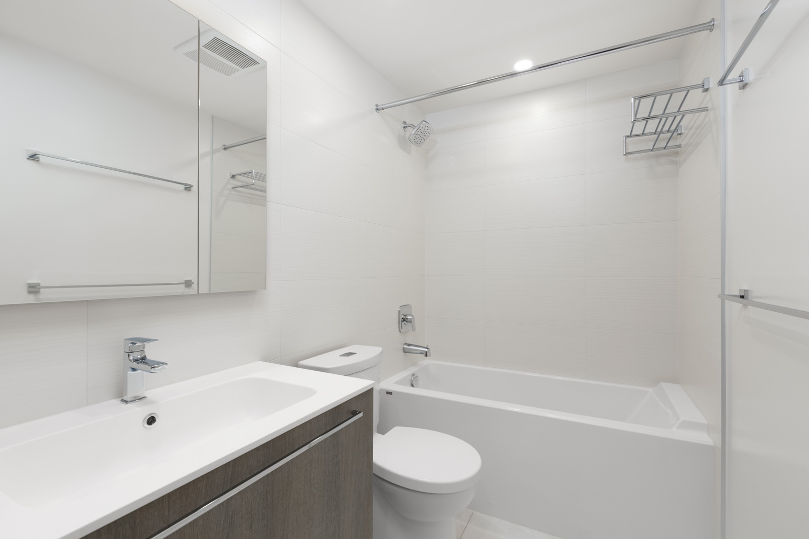 Modern bathroom with white bathtub, toilet, and sink. Wall-mounted cabinet with mirror. Chrome fixtures and towel bar. Minimalist design with neutral tones.