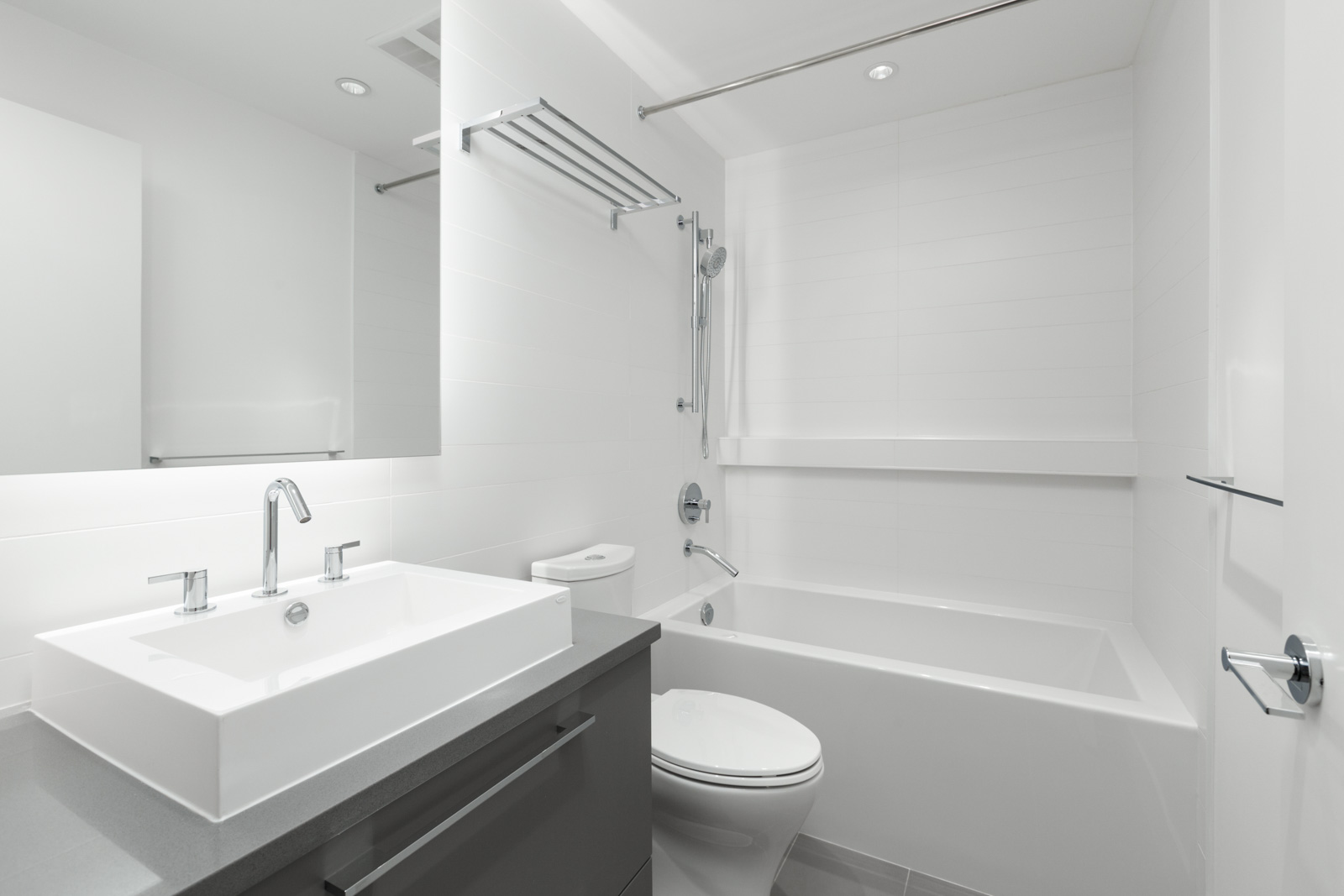 bathroom with vanity sink and mirror on left and tub and shower with tiled walls on right in bathroom of brand new condo managed by birds nest properties at kings crossing in burnaby