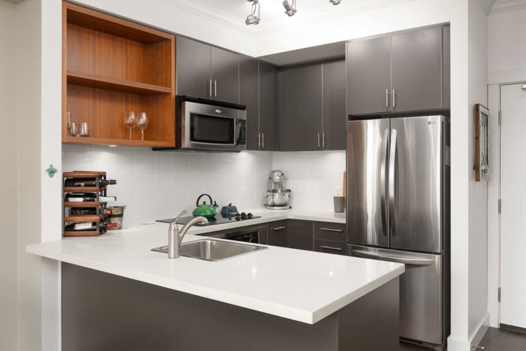 Modern kitchen with stainless steel fridge and microwave and granite countertops with storage cabinets in a rental condo in East Vancouver offered by Birds Nest Properties