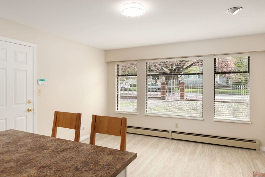 Living room area past the kitchen with large windows providing natural sunlight in a unit with ceiling lighting and laminate hardwood flooring in a rental home in East Vancouver provided by Birds Nest Properties