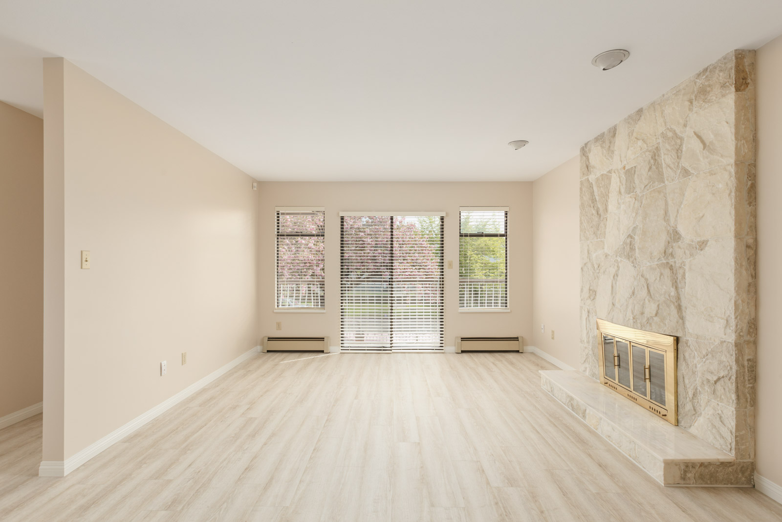 Spacious living area with natural sunlight from wall-to-wall windows and a fireplace to the right in an area with laminate hardwood flooring in a rental home in East Vancouver provided by Birds Nest Properties