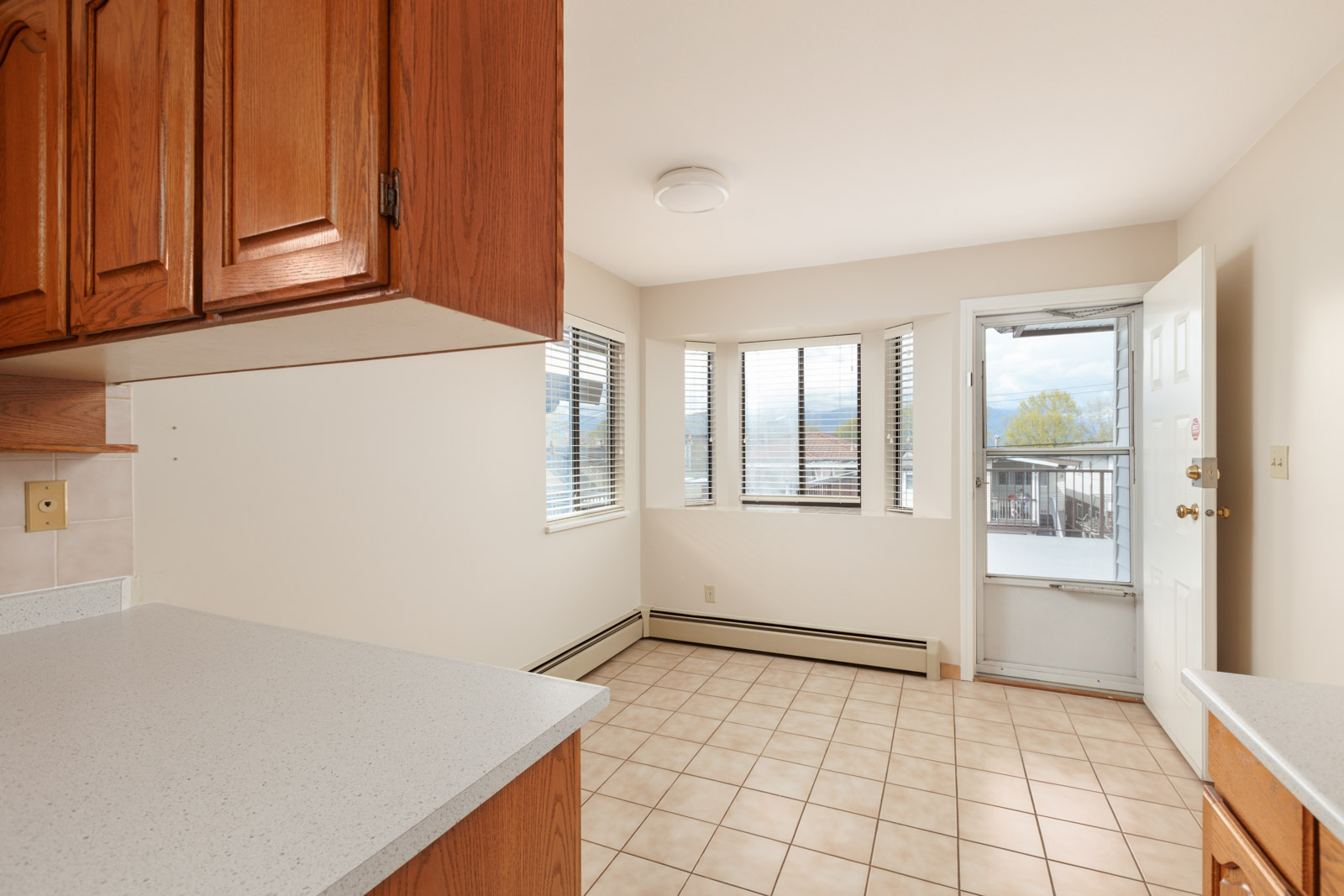 Spacious living area past the kitchen with tiled flooring and windows bring in natural sunlight, with a door to the balcony in a rental home in East Vancouver provided by Birds Nest Properties