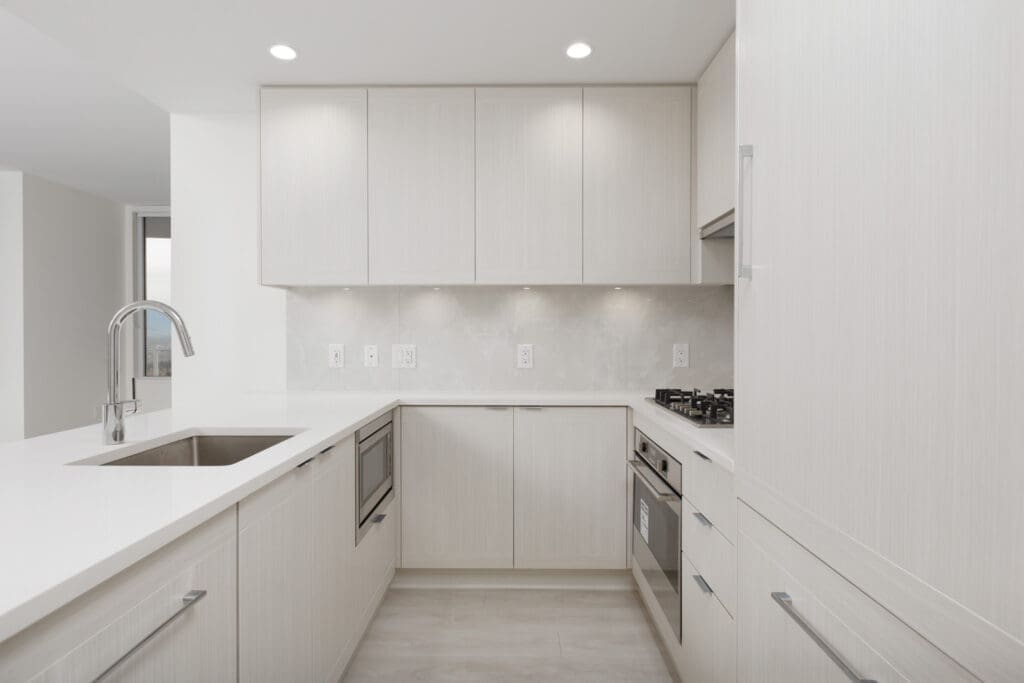 Modern kitchen with light-colored cabinets, built-in appliances, gas cooktop, under-cabinet lighting, and a stainless steel sink with a gooseneck faucet.