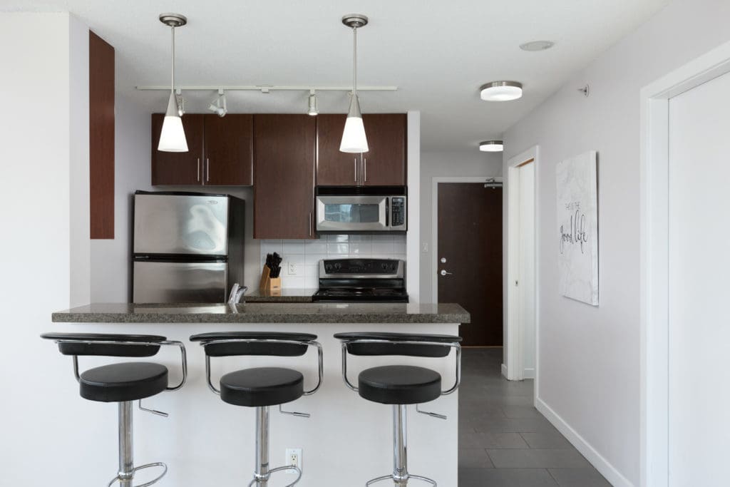 spacious kitchen with island and barstool seating with modern light fixtures above and high-end appliances in a rental condo in vancouver offered by Birds Nest Properties