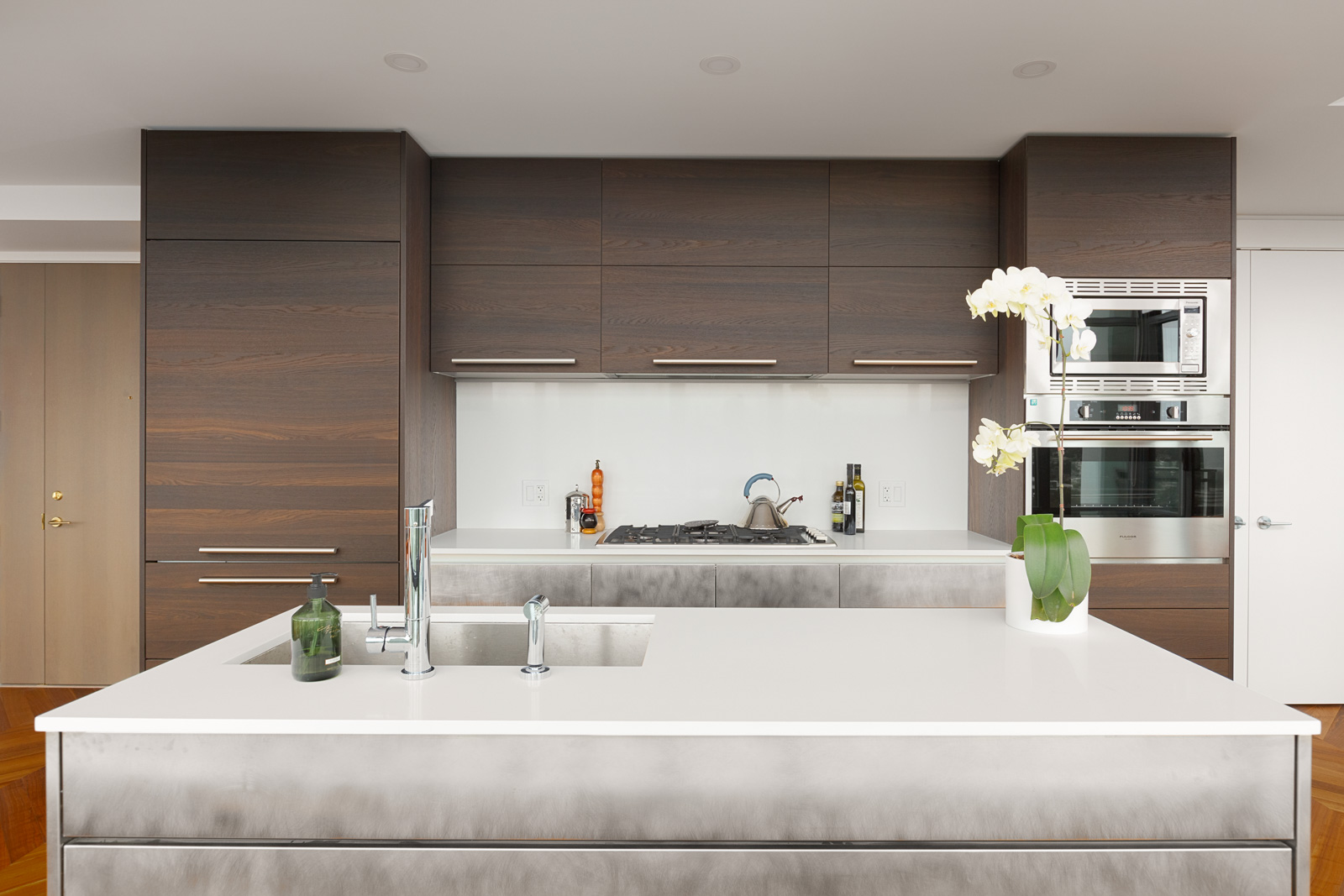 Modern kitchen with quartz countertops and high-end kitchen appliances, with natural gas cooktop, and stainless steel microwave and oven. Centered in the unit is a kitchen island, with a stainless steel sink, all located in a rental condo in Burnaby offered by Birds Nest Properties.