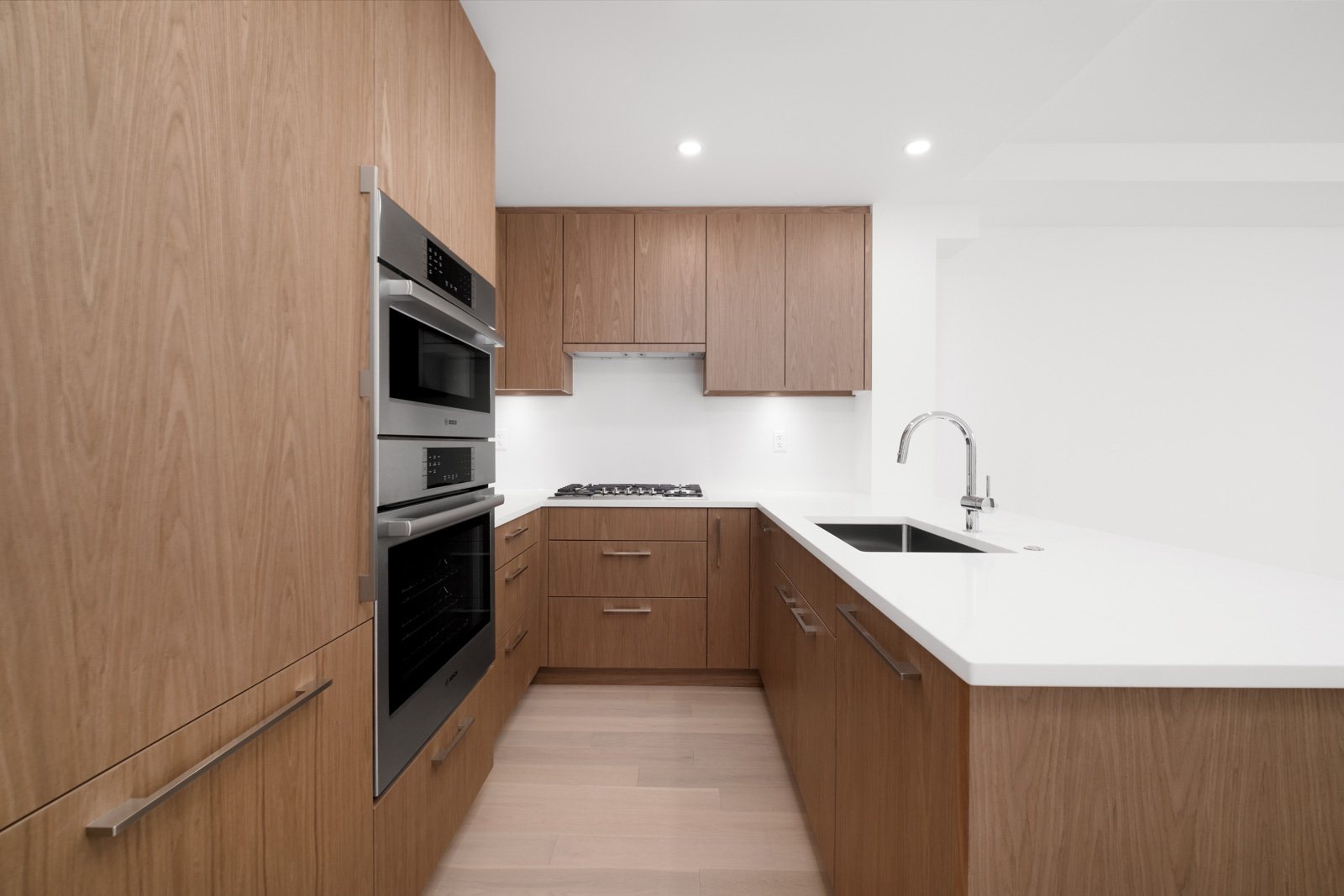 Modern kitchen with wood cabinets, built-in stainless steel appliances, white countertops, and a sink with a faucet on the island.