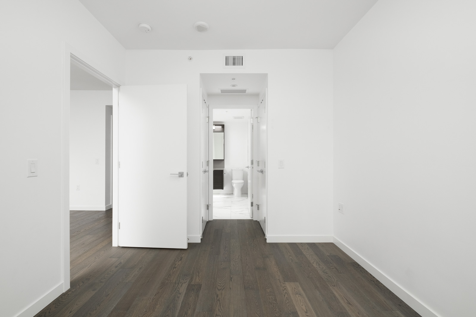 bedroom with door to closet and bathroom with hardlwood floors and white walls in navio building on pullman porter street in olympic village vancouver