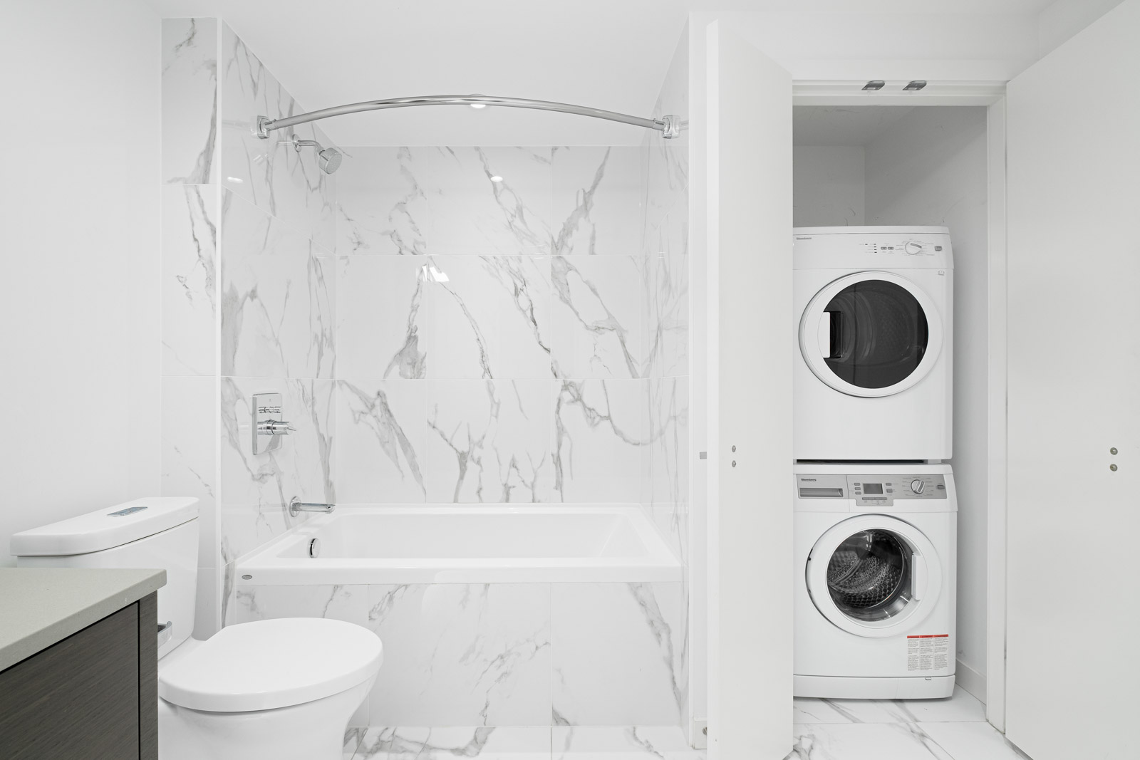 stacked white washer and dryer on right and bathroom on left with marble tiling in rental condo in navio