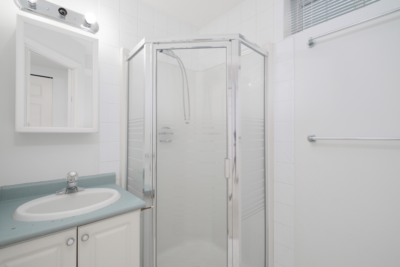 shower in corner of bathroom and vanity and mirror on left managed by birds nest properties in east vancouver