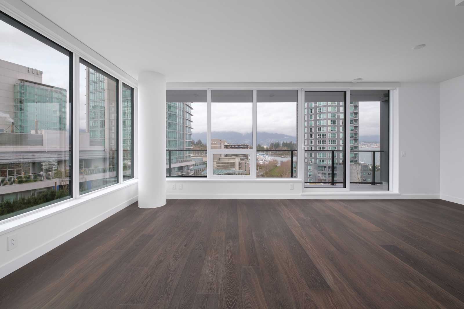 living room with wide windows in the background and on the left with white walls and dark hardwood flooring managed at cardero managed by birds nest properties