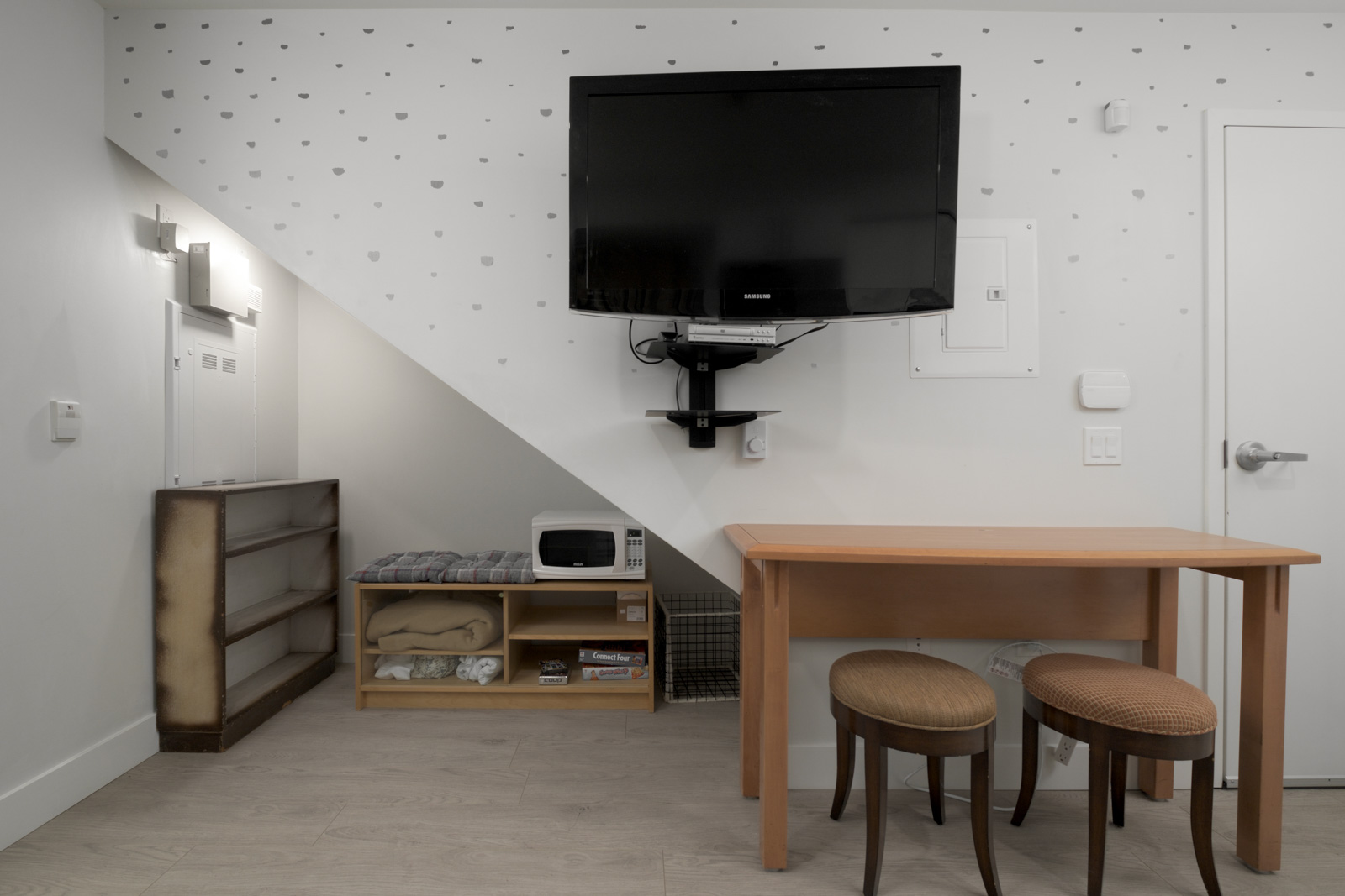 living room with tv embedded on the wall with brown table and stool with white walls at east vancouver