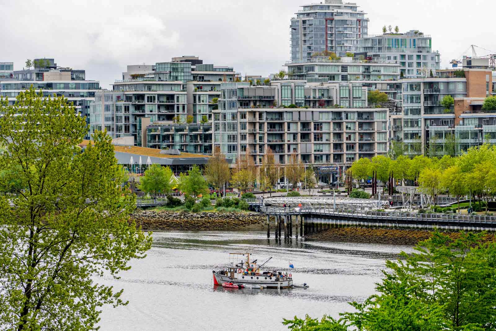 A fishing boat on a river with modern apartment buildings and greenery in the background.