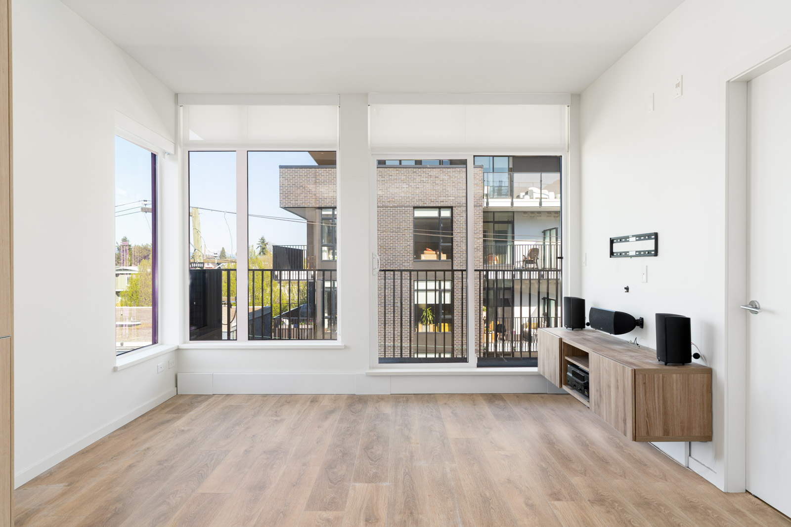 Open living area with media stand, hardwood floors, and large windows and balcony access