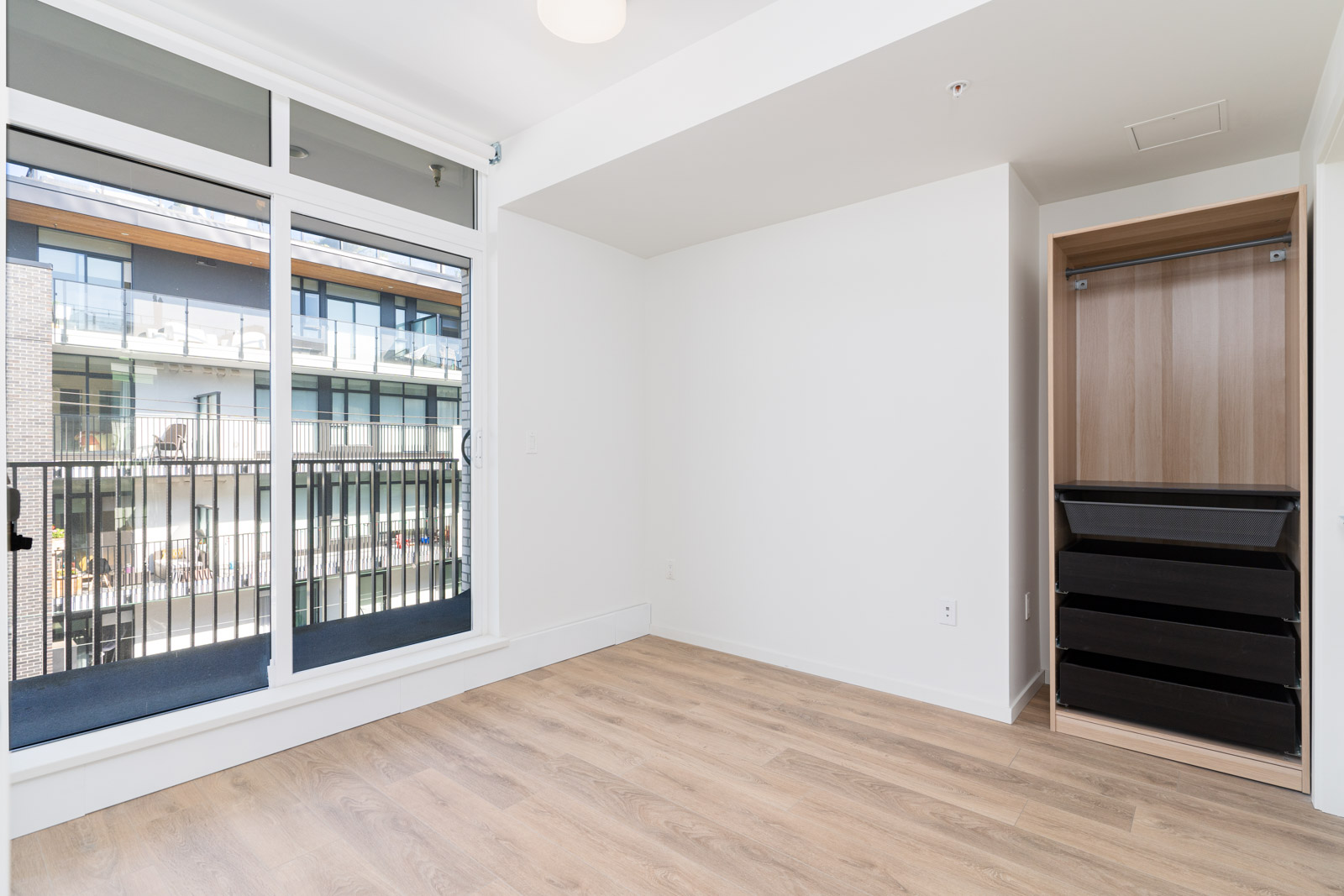 bedroom with large windows, balcony and open wardrobe with laminate floors