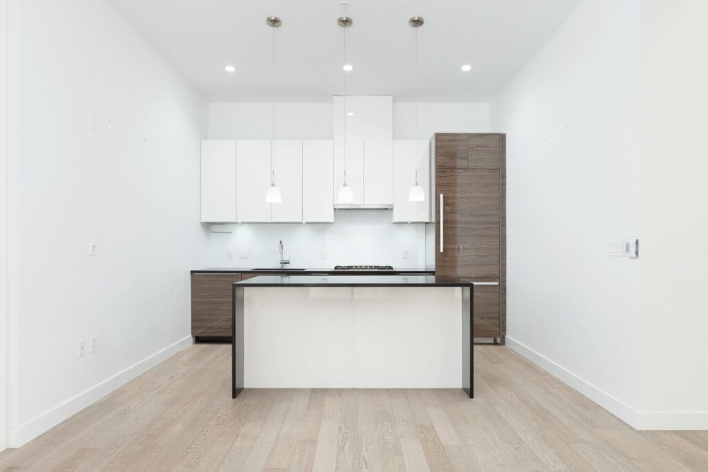 Modern, minimalist kitchen with white cabinets, wooden accents, a central island, pendant lights, and light wood flooring.