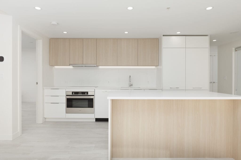 Minimalist kitchen with light wood cabinets, white countertops, and stainless steel appliances. Bright lighting and a central island enhance the clean and modern design.