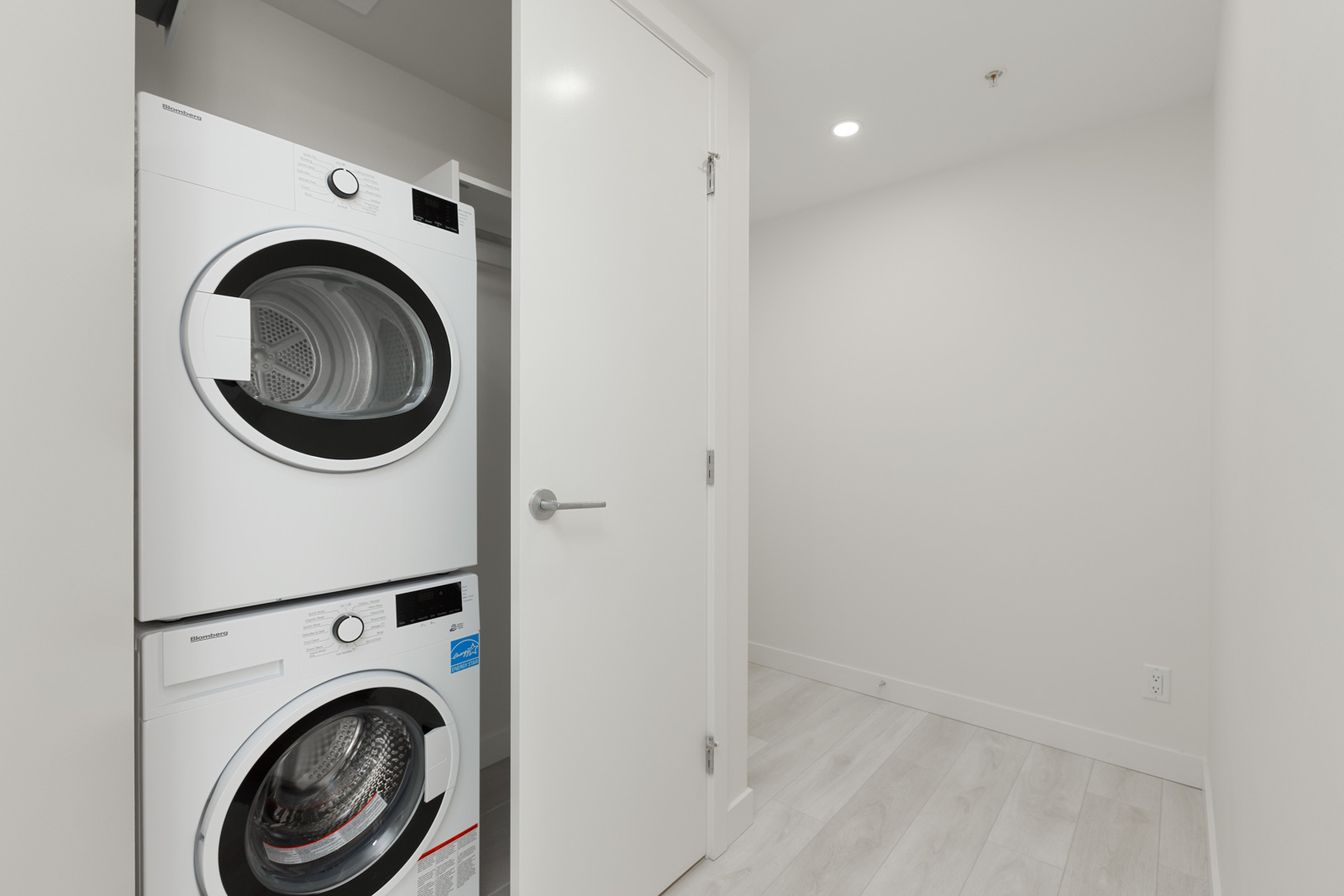Laundry room with stacked white washer and dryer in a small alcove with an open door.